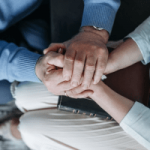 Group of people placing hands together in a circle to symbolize teamwork and unity.